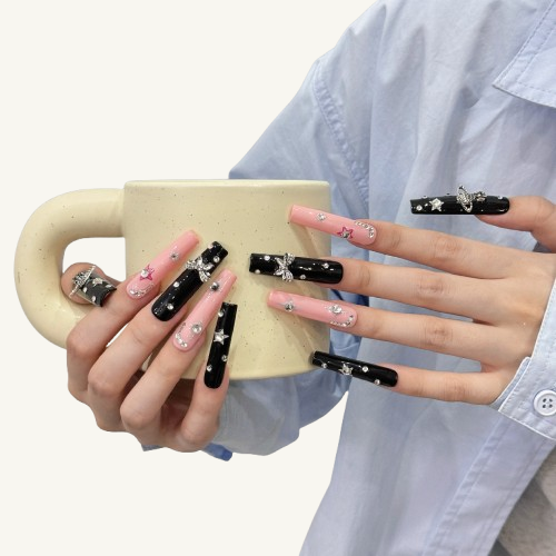 A set of long square Y2K punk style press-on nails in a pink and black theme, adorned with a 3D Saturn, bows, and star charms.
