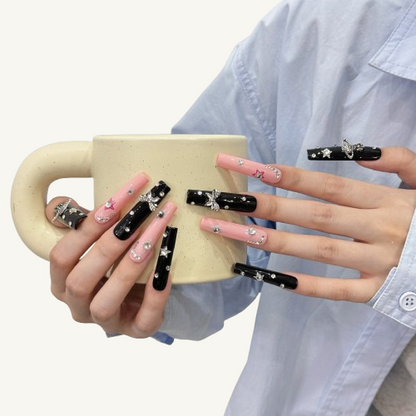 A set of long square Y2K punk style press-on nails in a pink and black theme, adorned with a 3D Saturn, bows, and star charms.
