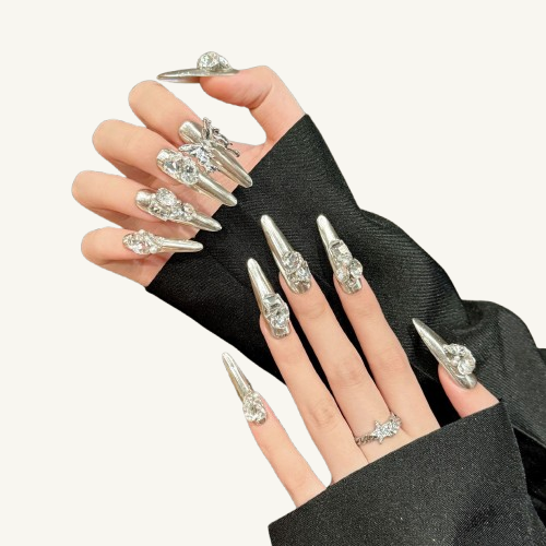 A set of long coffin press-on nails with a liquid metal silver base, adorned with luxury crystal clusters and a 3D metallic bow charm.