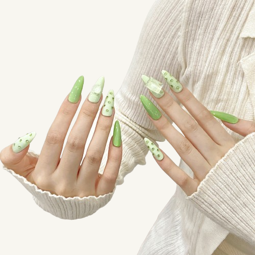 Hands wearing avocado green long stiletto press-ons with hand-set studs and a 3D irregular gem.