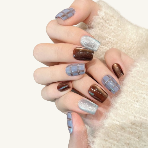 A handmade coffin press-on set mixing blue-grey plaid, brown cat-eye, and ice blue glitter designs.