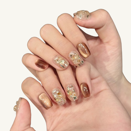 A set of short coffin press-on nails with a bronze cat-eye effect, paired with sheer nails featuring crushed shells and gold foil.