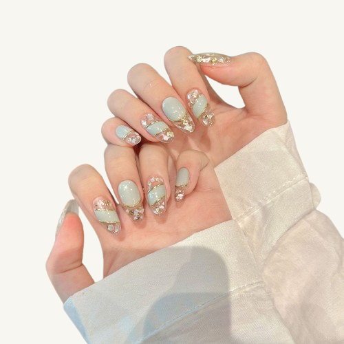 A geode-style set of handmade oval press-on nails, light blue and clear design with shell and gold foil inside, outlined with gold lines.