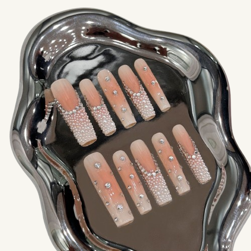 An extra-long set of baddie-style press-on nails with a nude ombre base, encrusted with pearls and ice-like rhinestones.
