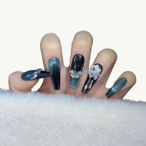 Hands wearing coffin press-on nails with a blue-black cat eye effect and luxury 3D crystal flower decorations.