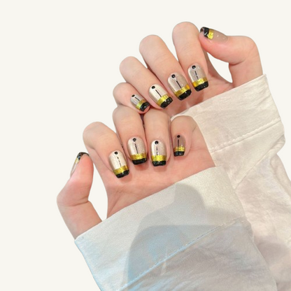 A geometric style set of handmade short coffin press-on nails featuring a silver-white cat-eye, black blocks, a wide gold band, and line art.