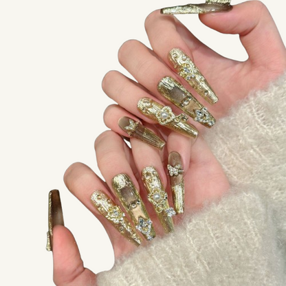 A luxury set of handmade long coffin press-on nails, featuring a carved gold texture and cat-eye effect, adorned with crystal crowns and pearls.