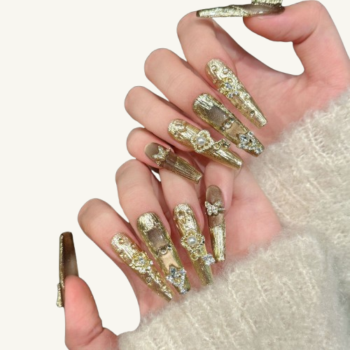 A luxury set of handmade long coffin press-on nails, featuring a carved gold texture and cat-eye effect, adorned with crystal crowns and pearls.