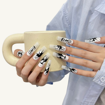 A set of long square press-on nails with black  graffiti art over an icy grey-white base, accented with sparkling crystals.