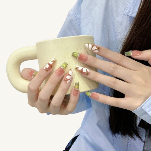 Hands displaying Green Field Flora style handmade press-on nails, featuring painted white flowers and green French tips with rhinestones on ballet nails.