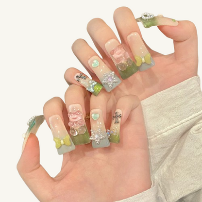 A set of handmade long square press-on nails, matcha green glitter gradient, adorned with a pink jelly bear, bow, pearl heart and other charms.