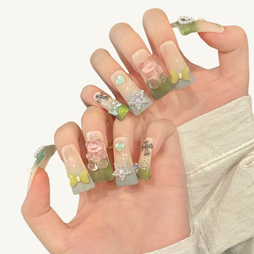 A set of handmade long square press-on nails, matcha green glitter gradient, adorned with a pink jelly bear, bow, pearl heart and other charms.