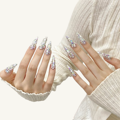 A pair of hands wearing XXL stiletto press-on nails, with the nails covered in ice-crystal-like aurora rhinestones.