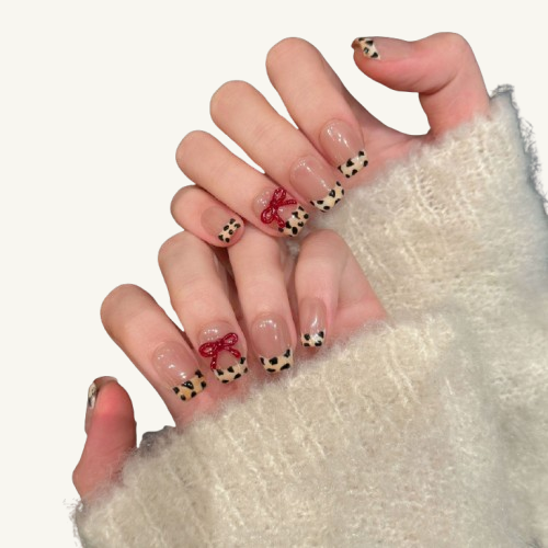 A sweet-and-edgy style handmade coffin press-on set, milk-tea nude base with a leopard French tip and a red bow.