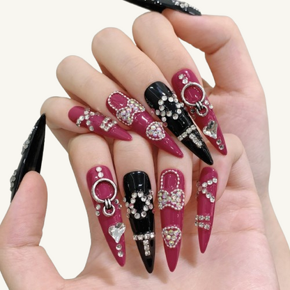 A dark fairytale style handmade stiletto press-on set, pink and black palette, inlaid with abundant crystals, hearts, and bows.