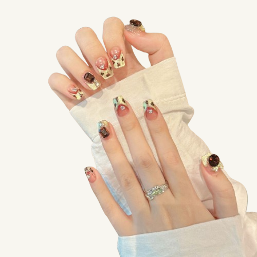 A set of handmade press-on nails with champagne gold leopard cat-eye, adorned with a large dark red jewel and a gold bow.