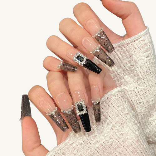 A set of handmade long coffin press-on nails with translucent black French tips, a pearl and crystal smile line, and a massive black gem.