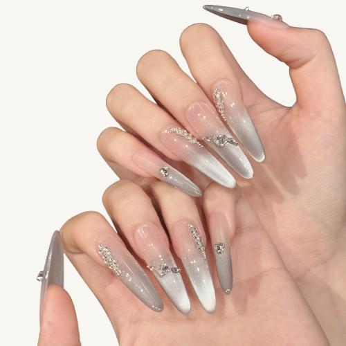 A set of handmade stiletto press-on nails, pink-to-grey cat-eye gradient, and adorned with leaf patterns made of marquise crystals.