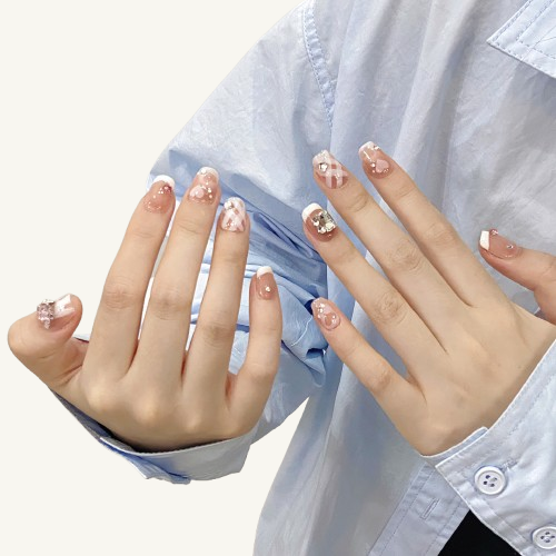 Hands wearing short press-on nails with a pink and white plaid pattern, French tips, and pink diamond decorations.