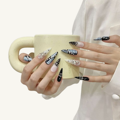 A set of punk style long stiletto press-on nails in a black and white theme, featuring 3D embossed silver beads and a Baroque cross.