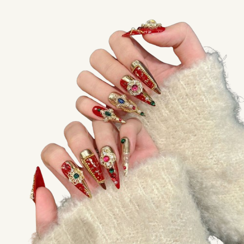 Hands wearing red, green, and gold holiday-themed long stiletto press-on nails, inlaid with large gems and gold decor.