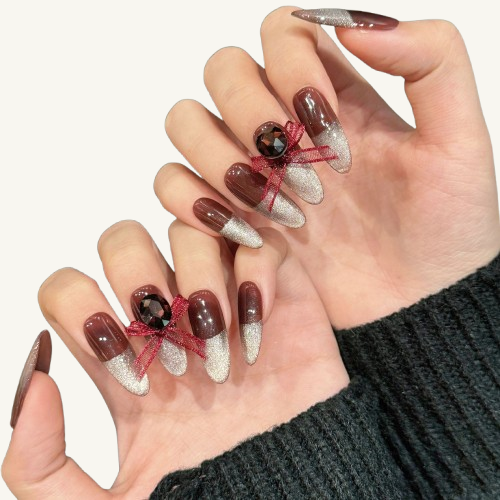 A red wine party themed handmade oval press-on nails set, combining reddish-brown and silver glitter, adorned with a red bow and a smoky gem.