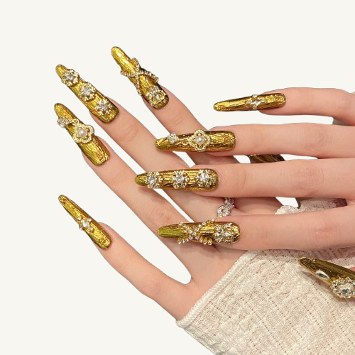 A Rococo style handmade stiletto press-on set, carved gold, adorned with heart crystals, snowflakes, and a pearl clover dangle.