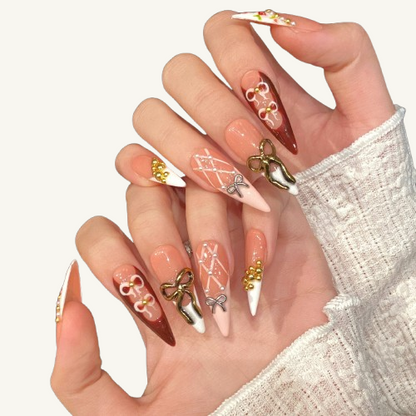 A set of handmade stiletto press-on nails, mixing designs of hand-painted roses, bows, pearls, and gold beads in a gentle color palette.