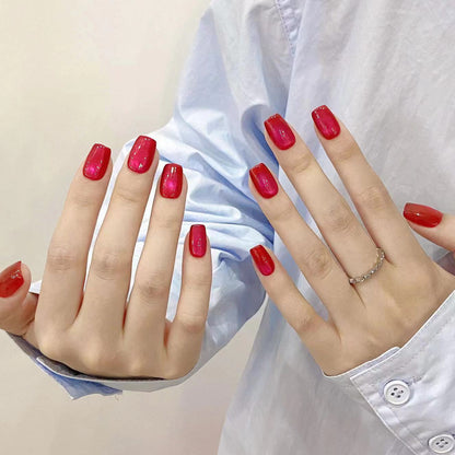 Hands wearing classic ruby red cat eye press-on nails in a short oval shape, against a blue shirt background.