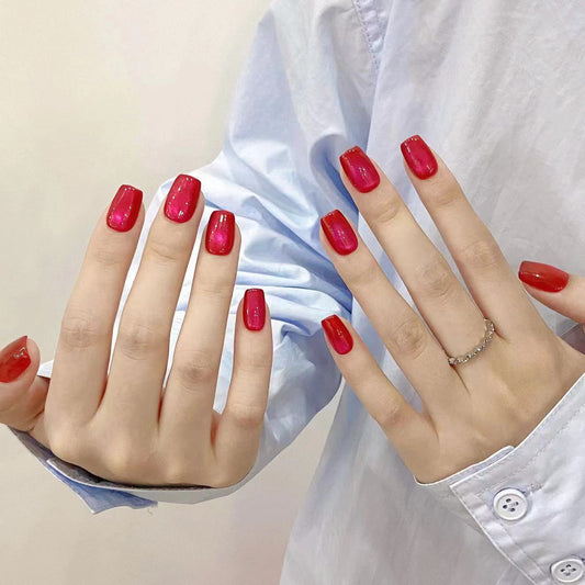 Hands wearing classic ruby red cat eye press-on nails in a short oval shape, against a blue shirt background.