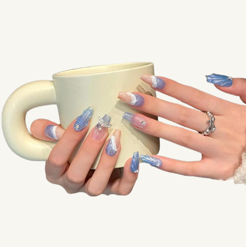 A set of wave and sand textured press-on nails in light blue glitter and blush pink, with a mermaid tail and rhinestone charms.

