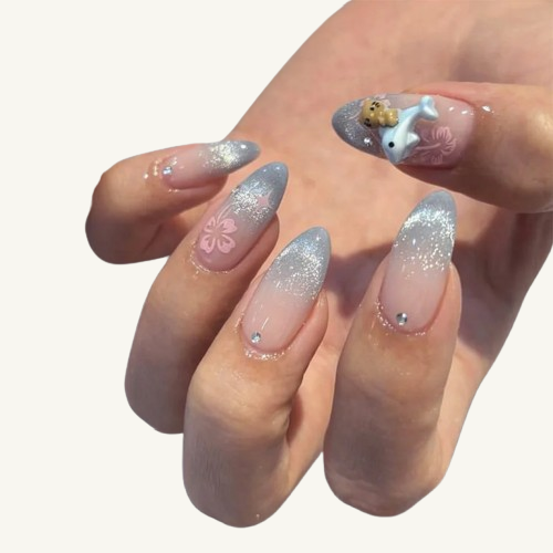 Two hands wearing a set of long almond press-on nails with a silver-grey cat-eye ombre, adorned with 3D dolphin, bear, and floral patterns.