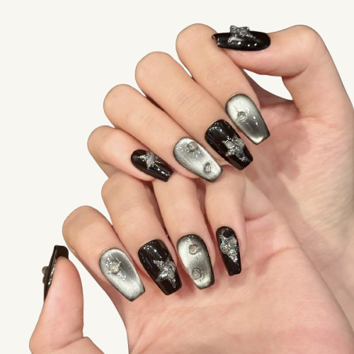 A set of handmade coffin press-on nails with a black and silver cat-eye base, featuring a starburst effect made of moonstone fragments and glitter.