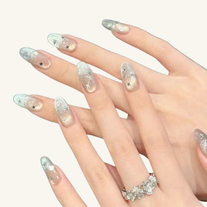A set of handmade champagne gold to silver gradient cat-eye press-on nails with silver star decorations and thread details, oval shape.