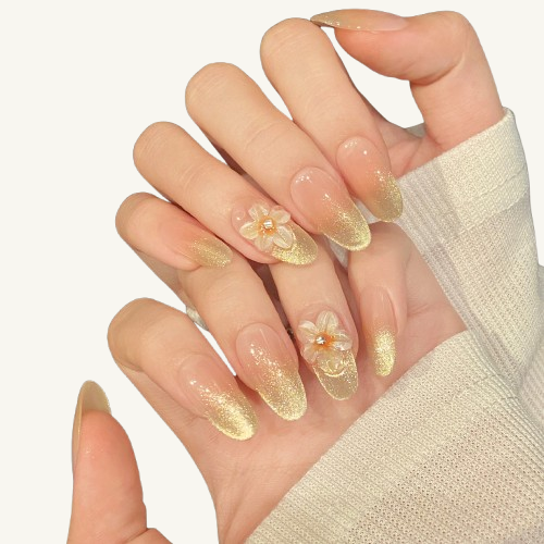 A set of handmade press-on nails, peach nude to gold glitter gradient, and adorned with a 3D glass-textured flower.