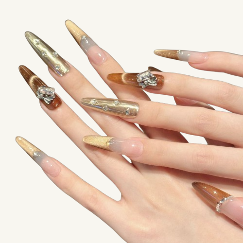 A set of handmade stiletto press-on nails featuring a toffee-colored cat-eye French tip, adorned with crystals, pearls, and a bow.