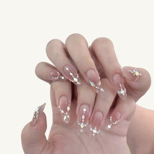 A hand wearing V-cut crystal French design press-on nails, with geometric crystal lines and draping decorations on a nude ombre base.