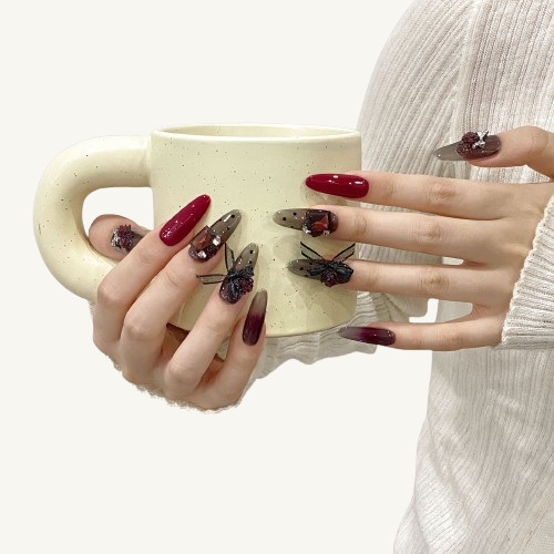 A set of long almond press-on nails with a smoky grey polka dot design, adorned with 3D wine-red roses, a gemstone, and bows.
